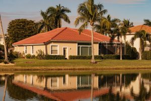 A beautiful summer house in South Florida on a sunny day. Typical concrete house on the shore of a lake in southwest Florida in the countryside with palm trees, tropical plants and flowers, lawn and pine trees. Florida.